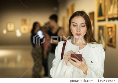 While visiting museum, girl uses travel guide application on her phone. While visiting museum, girl uses travel guide application on her phone. 139655687