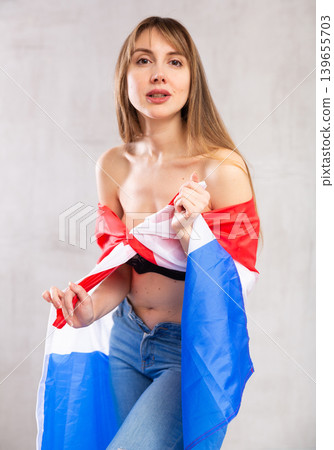 Flirting young woman posing with flag of Netherlands against gray wall background 139655703