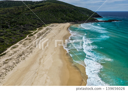 Aerial drone view of Seven Mile Beach in Forster showcasing a long stretch of sandy shoreline with ocean waves and surrounding natural coastal landscape. Aerial drone view of Seven Mile Beach in Forster showcasing a long stretch of sandy shoreline with ocean waves and surrounding natural coastal landscape. 139656026