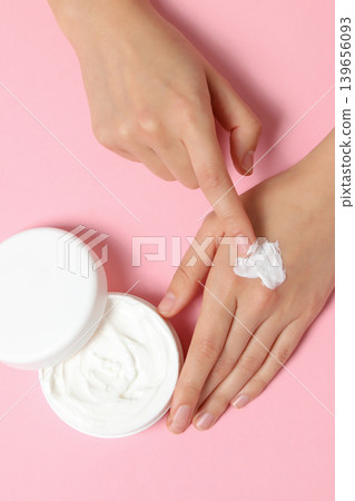 Hand applying cream from container on pink surface Hand applying cream from container on pink surface 139656093