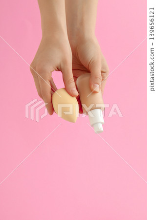 Hands hold a beauty sponge and a tube of cream against pink wall Hands hold a beauty sponge and a tube of cream against pink wall 139656121