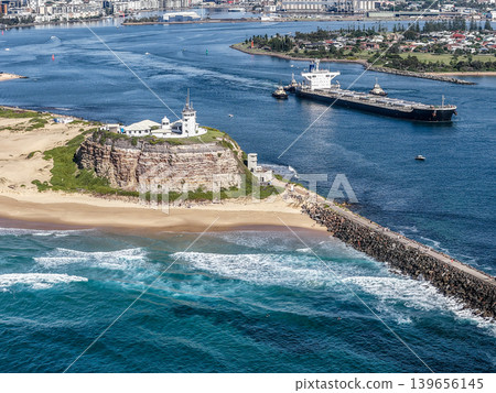 Aerial drone view of Nobbys Lighthouse and Nobbys Beach with a large cargo ship being escorted by tug boats through Newcastle Harbour in the background. Aerial drone view of Nobbys Lighthouse and Nobbys Beach with a large cargo ship being escorted by tug boats through Newcastle Harbour in the background. 139656145