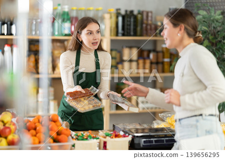 Female seller offers to buy candies to woman in interior of grocery supermarket Female seller offers to buy candies to woman in interior of grocery supermarket 139656295