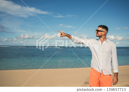 Man stands on sand, looking out at the water and pointing Man stands on sand, looking out at the water and pointing 139657713