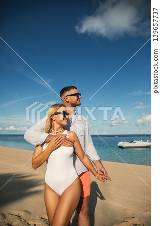 Couple stands together on sandy beach while looking at sea Couple stands together on sandy beach while looking at sea 139657737