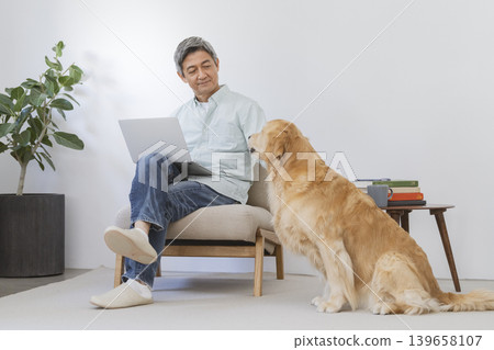 一位老年男子正在使用筆記型電腦，旁邊還有一隻金毛犬。 139658107