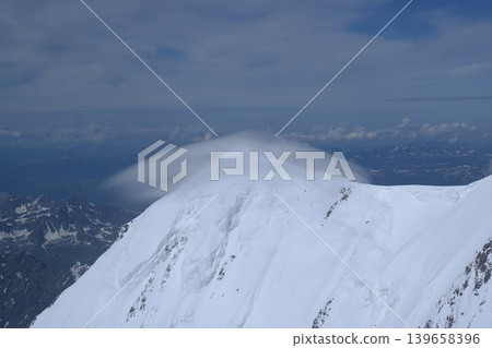 A stunning rock formation covered in snow, set against a clear blue sky with fluffy clouds in the background, creating a peaceful and breathtaking mountain landscape. 139658396