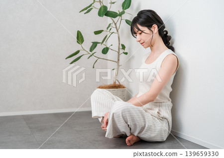 A young Asian woman in a tank top sits on the floor, troubled and contemplating (feeling insecure, stressed, depressed). A young Asian woman in a tank top sits on the floor, troubled and contemplating (feeling insecure, stressed, depressed). 139659330