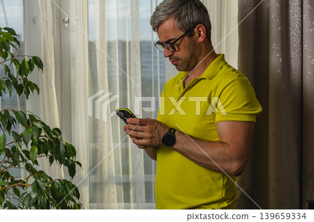 Man using smartphone beside window at home 139659334