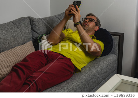 Man lying on sofa while browsing social media 139659336