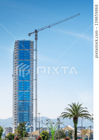 A modern high-rise building under construction with a tall crane, against a clear sky A modern high-rise building under construction with a tall crane, against a clear sky 139659868
