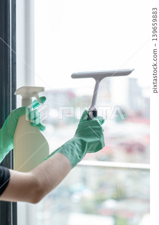 Washing the window with a gloved scraper and a spray bottle of detergent, removing water droplets  139659883