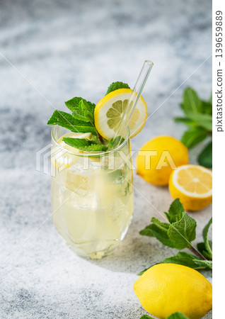 A summer drink with lemon, mint, and ice in a glass on a concrete background. A summer drink with lemon, mint, and ice in a glass on a concrete background. 139659889