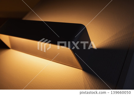 A warm modern wall sconce emits soft ambient light, casting dramatic shadows A warm modern wall sconce emits soft ambient light, casting dramatic shadows 139660050