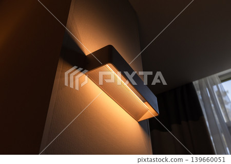 A modern wall sconce emits warm ambient light across a textured wall 139660051