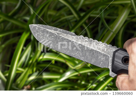 Hand grips a heavy stonewashed survival knife with a sawback spine Hand grips a heavy stonewashed survival knife with a sawback spine 139660060