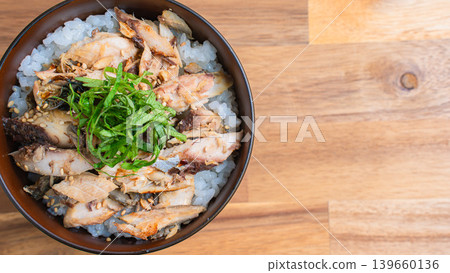 Grilled mackerel rice bowl with shredded mackerel and shiso leaves, served on a wooden table. 139660136