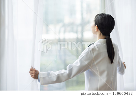 A Japanese female doctor in a white coat opens the curtain. 139660452