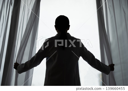 The silhouette of a female doctor in a white coat opening a curtain. The silhouette of a female doctor in a white coat opening a curtain. 139660455