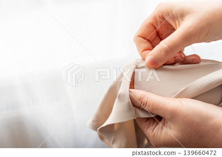 Woman darning a beige clothes by hand with needle and patch fabric Woman darning a beige clothes by hand with needle and patch fabric 139660472