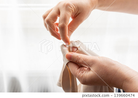 Woman darning a beige clothes by hand with needle and patch fabric Woman darning a beige clothes by hand with needle and patch fabric 139660474
