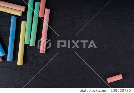 Colorful chalks pile on black background, different colors crayons on dark stone plate Colorful chalks pile on black background, different colors crayons on dark stone plate 139660720
