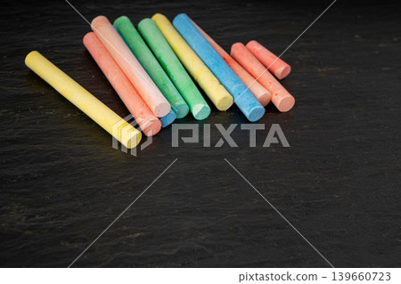 Colorful chalks pile on black background, different colors crayons on dark stone plate Colorful chalks pile on black background, different colors crayons on dark stone plate 139660723