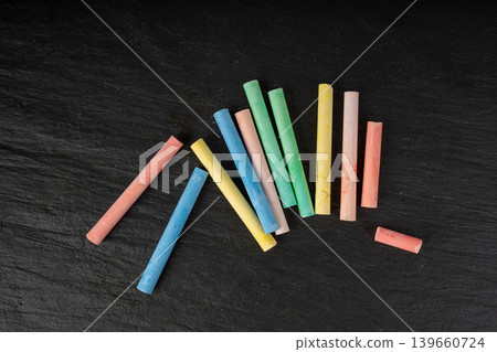 Colorful chalks pile on black background, different colors crayons on dark stone plate Colorful chalks pile on black background, different colors crayons on dark stone plate 139660724