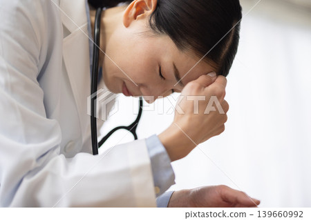 一位身穿白大褂的日本女醫生摸了摸太陽穴，露出痛苦的表情。 139660992