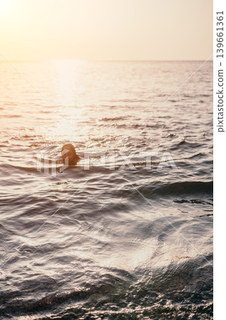 Woman swimming sunset young woman swims in the calm ocean water during a golden hour sunset with shimmering reflections Woman swimming sunset young woman swims in the calm ocean water during a golden hour sunset with shimmering reflections 139661361
