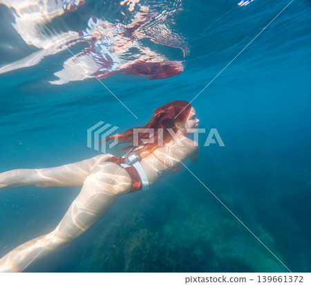 Woman swimming underwater as she explores the deep blue ocean during a bright summer day to find peace and adventure 139661372