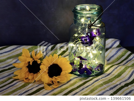 Glass jar filled with fairy lights on striped fabric with sunflowers Glass jar filled with fairy lights on striped fabric with sunflowers 139661506