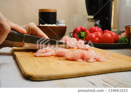Slicing raw chicken on a wooden cutting board in a kitchen setting with fresh vegetables Slicing raw chicken on a wooden cutting board in a kitchen setting with fresh vegetables 139661835