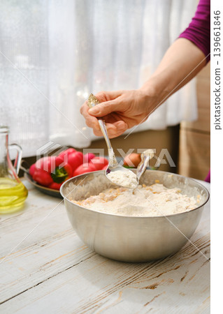 Mixing flour in a large bowl for baking in a sunny kitchen with fresh vegetables on the table Mixing flour in a large bowl for baking in a sunny kitchen with fresh vegetables on the table 139661846