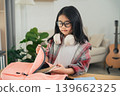Young girl with glasses and headphones preparing for school, looking inside pink backpack on desk in cozy room with guitar 139662325