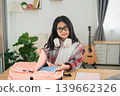 Smiling Young Girl Preparing for School with Backpack and Headphones in a Bright and Cozy Study Room with Guitar in the Background 139662326