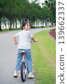 Young girl riding bicycle in park with green grass and trees, enjoying outdoor activity, leisure time, and joyful moment on a sunny day 139662337