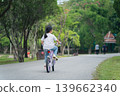 Child Riding Bicycle in Serene Park Setting Surrounded by Lush Green Trees and Pathway Ideal for Family Outdoor Activities and Leisure Time 139662340