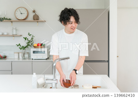 一位年輕的亞洲男子正在廚房洗碗。 一位年輕的亞洲男子正在廚房洗碗。 139662410