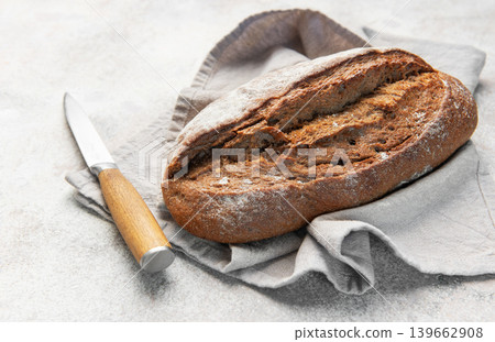 Rustic dark bread loaf with knife on napkin Rustic dark bread loaf with knife on napkin 139662908