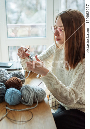 Woman knitting with yarn by window at home Woman knitting with yarn by window at home 139662937