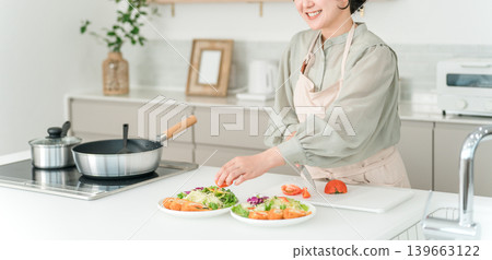 年輕的亞裔女子穿著圍裙在廚房做飯 年輕的亞裔女子穿著圍裙在廚房做飯 139663122
