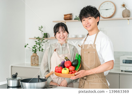 一對年輕的亞裔男女在廚房裡拿著蔬菜，他們是夫妻。 139663369
