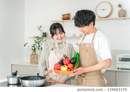 一對年輕的亞裔男女在廚房裡拿著蔬菜,他們是夫妻。 一對年輕的亞裔男女在廚房裡拿著蔬菜,他們是夫妻。 139663370