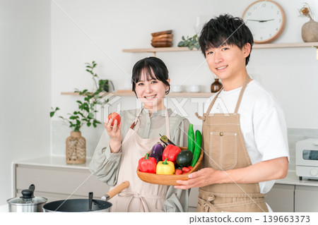 A young Asian couple holding tomatoes in the kitchen. A young Asian couple holding tomatoes in the kitchen. 139663373