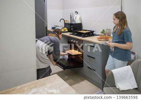 Attractive daughter and mother cooking italian pizza together in cozy domestic kitchen. Attractive daughter and mother cooking italian pizza together in cozy domestic kitchen. 139663598