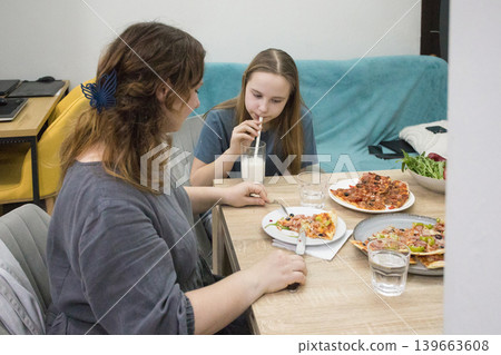 Cute child girl drinking milk and eating pizza with mother Cute child girl drinking milk and eating pizza with mother 139663608
