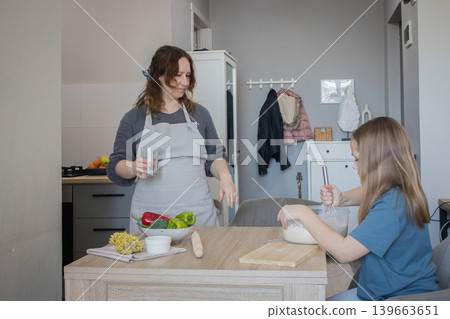 Cheerful mother and young daughter cooking together Cheerful mother and young daughter cooking together 139663651