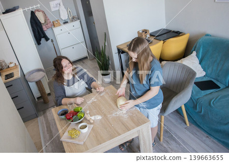 Lifestyle portrait of child girl preparing dough with her mother at home 139663655