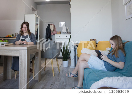 Lifestyle portrait of child girl using a tablet gadget while her mother does housework at home Lifestyle portrait of child girl using a tablet gadget while her mother does housework at home 139663659